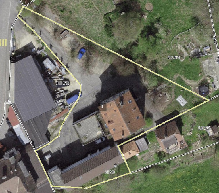 Aerial view of a property with several buildings, including a large building with a gray roof, a smaller building with a brown roof, and a building with a red roof. The property is surrounded by a yellow line indicating the boundaries.