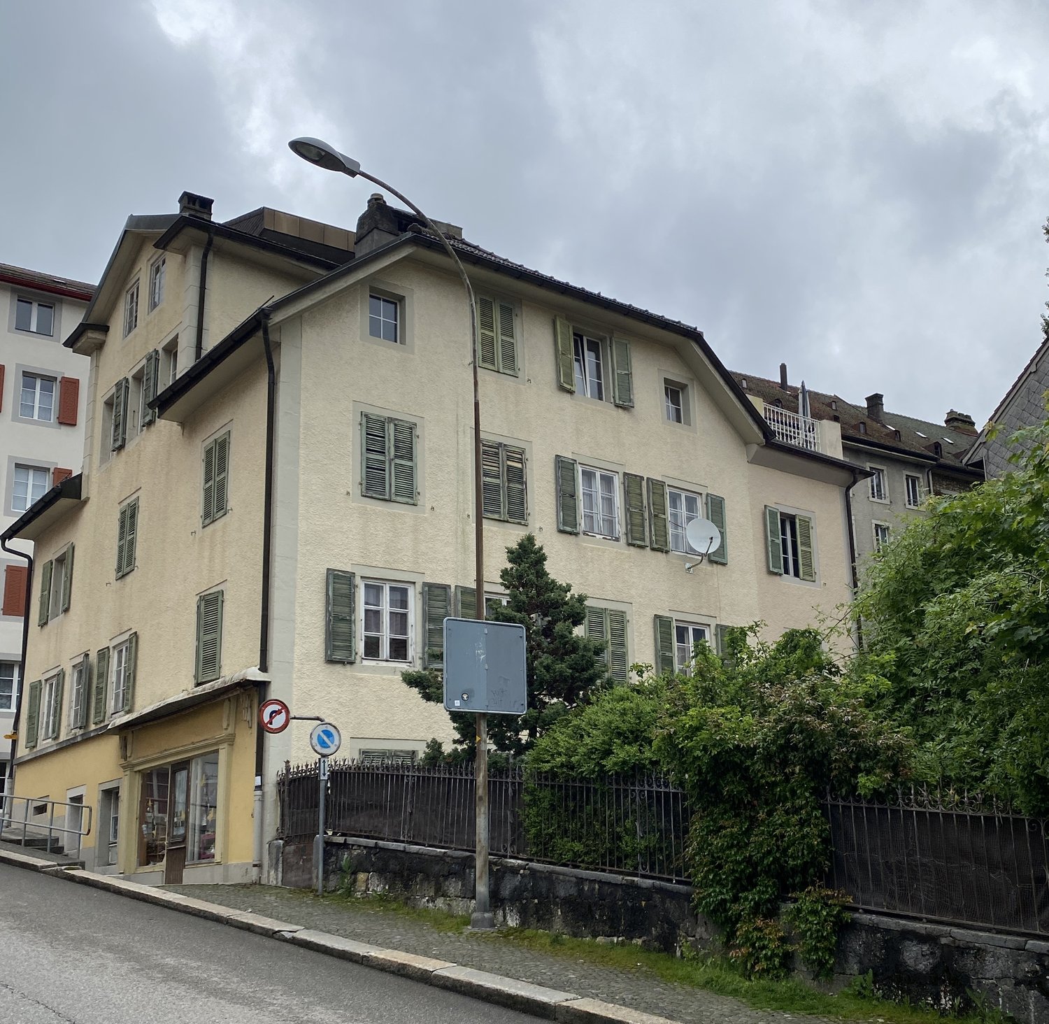3 story building, beige exterior, multiple windows, green shutters, street light, fence, plants