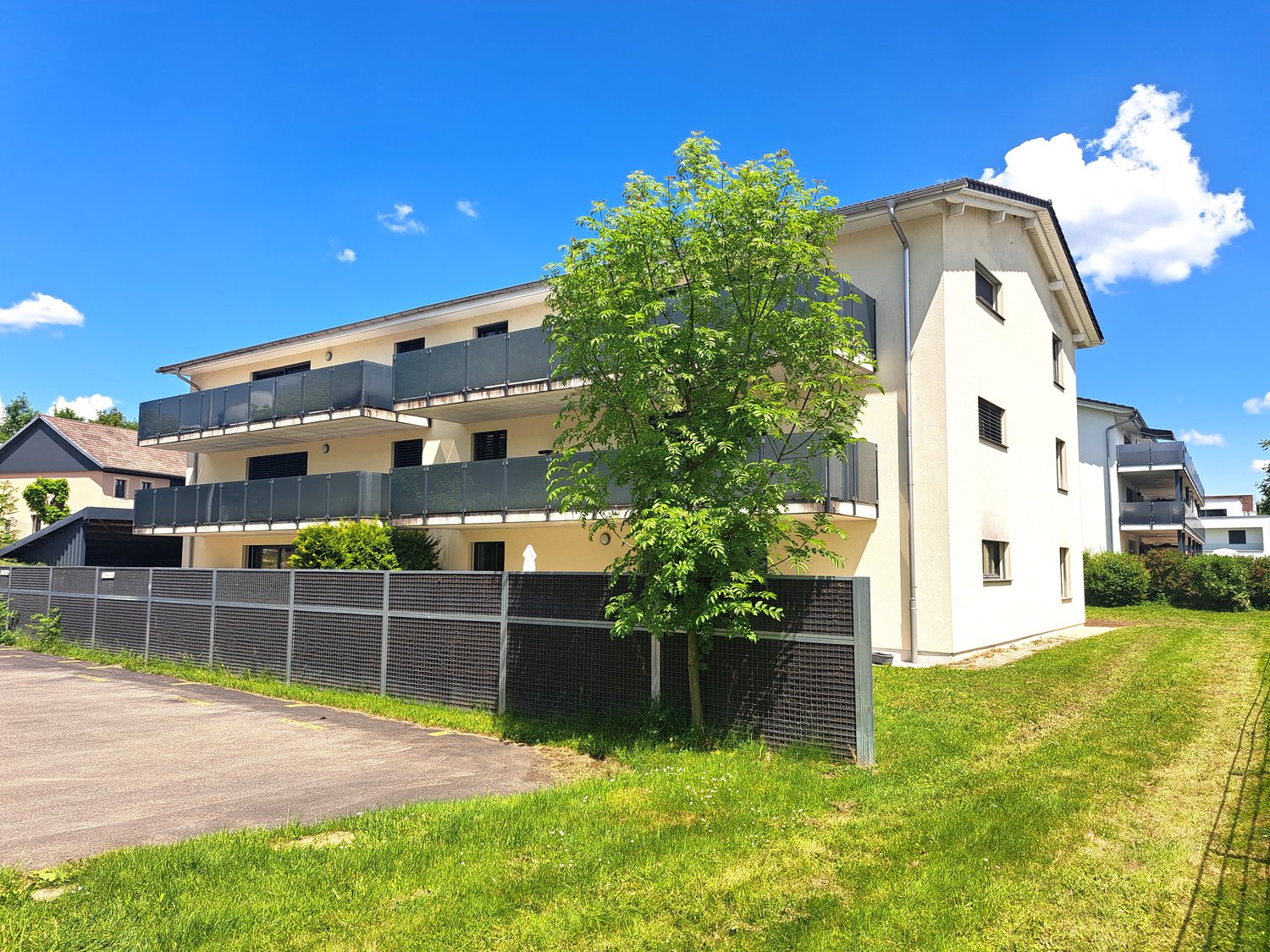 3-story apartment building with balconies, surrounded by green grass and trees