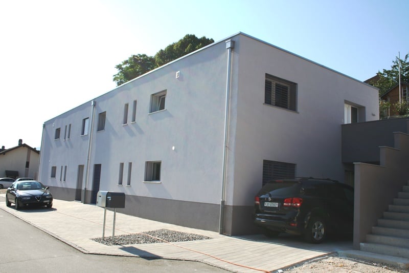 2 story building, white facade, 6 windows, 2 cars parked in front and garage
