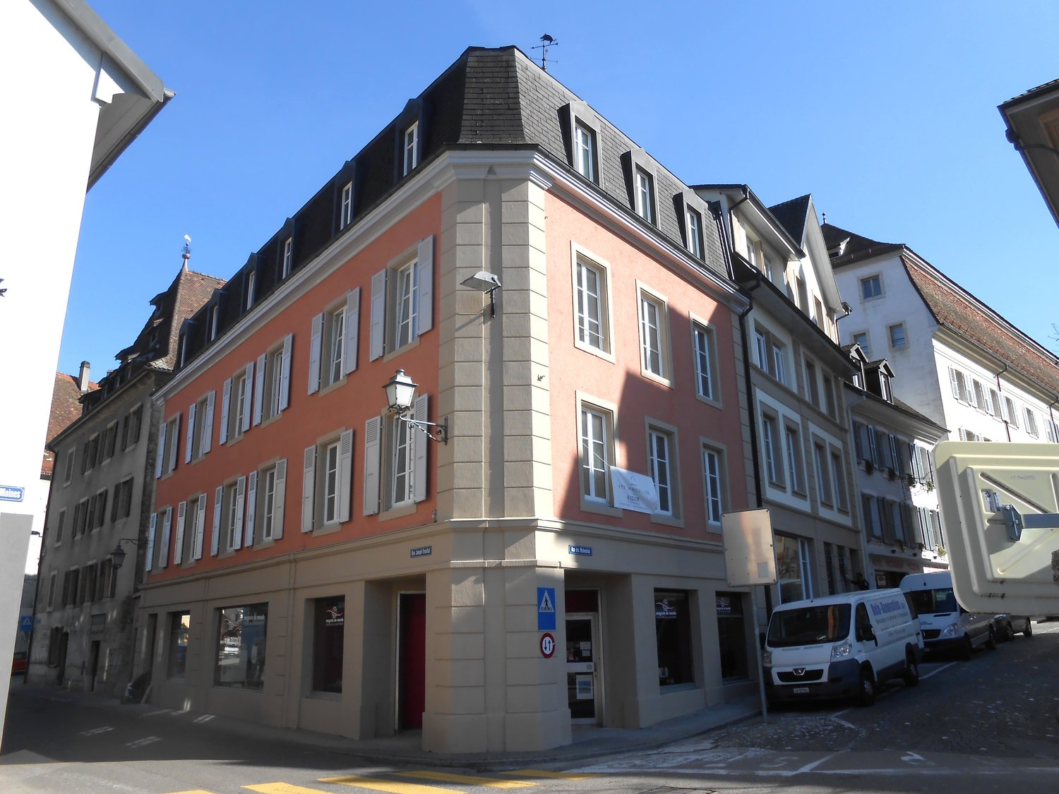 5-story building, red brick, white shutters, several windows, lamp on wall, multiple vans parked
