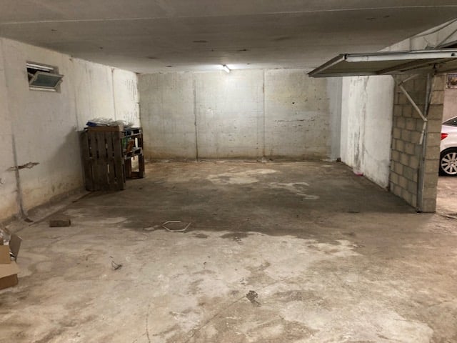 Empty parking area with concrete floor, brick wall, single car entrance, metal door, small window, car in front of garage.