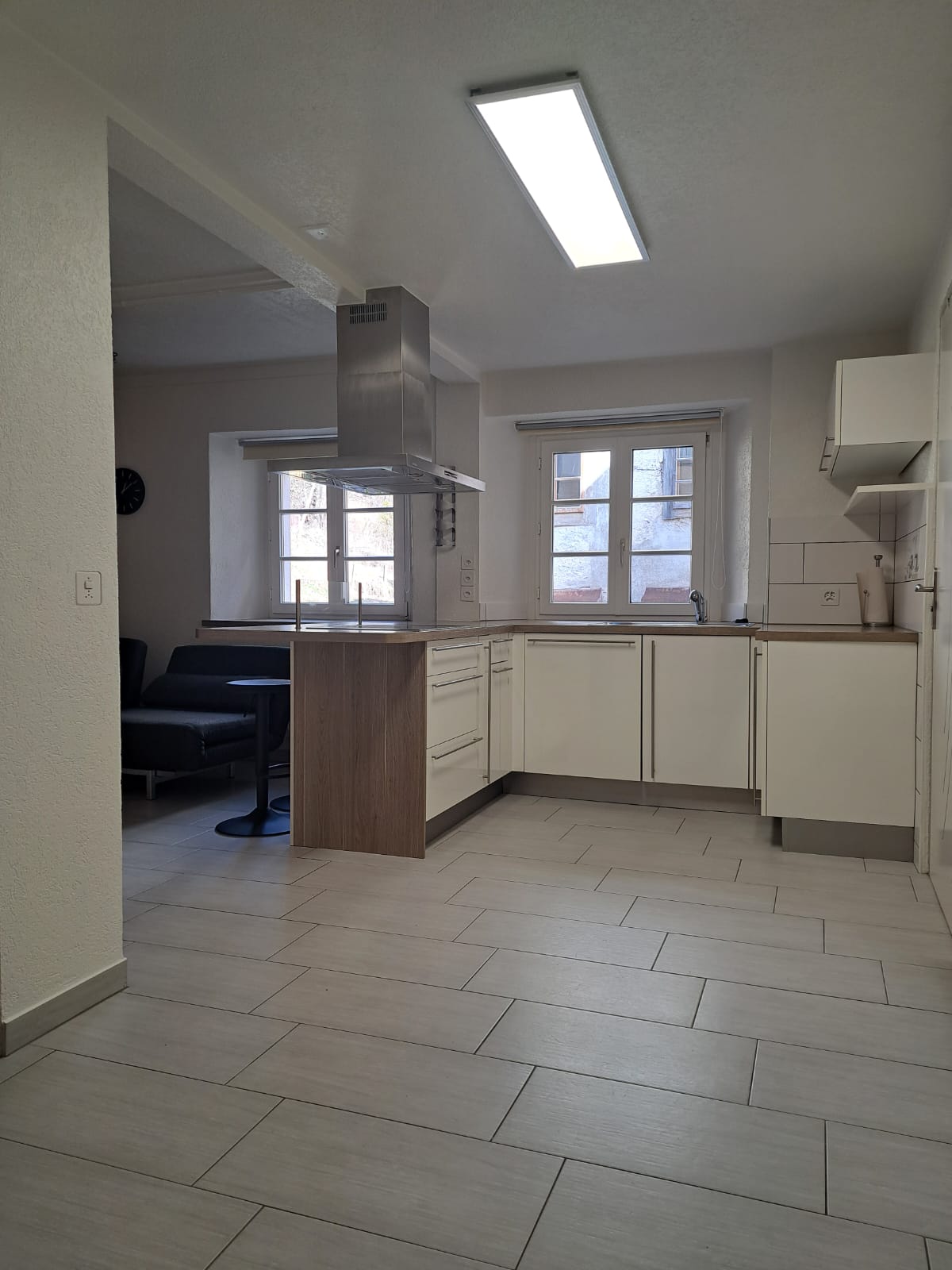 Modern kitchen with island, white cabinets, central island, sink with faucet, kitchen windows, tiled floor, overhead lighting.