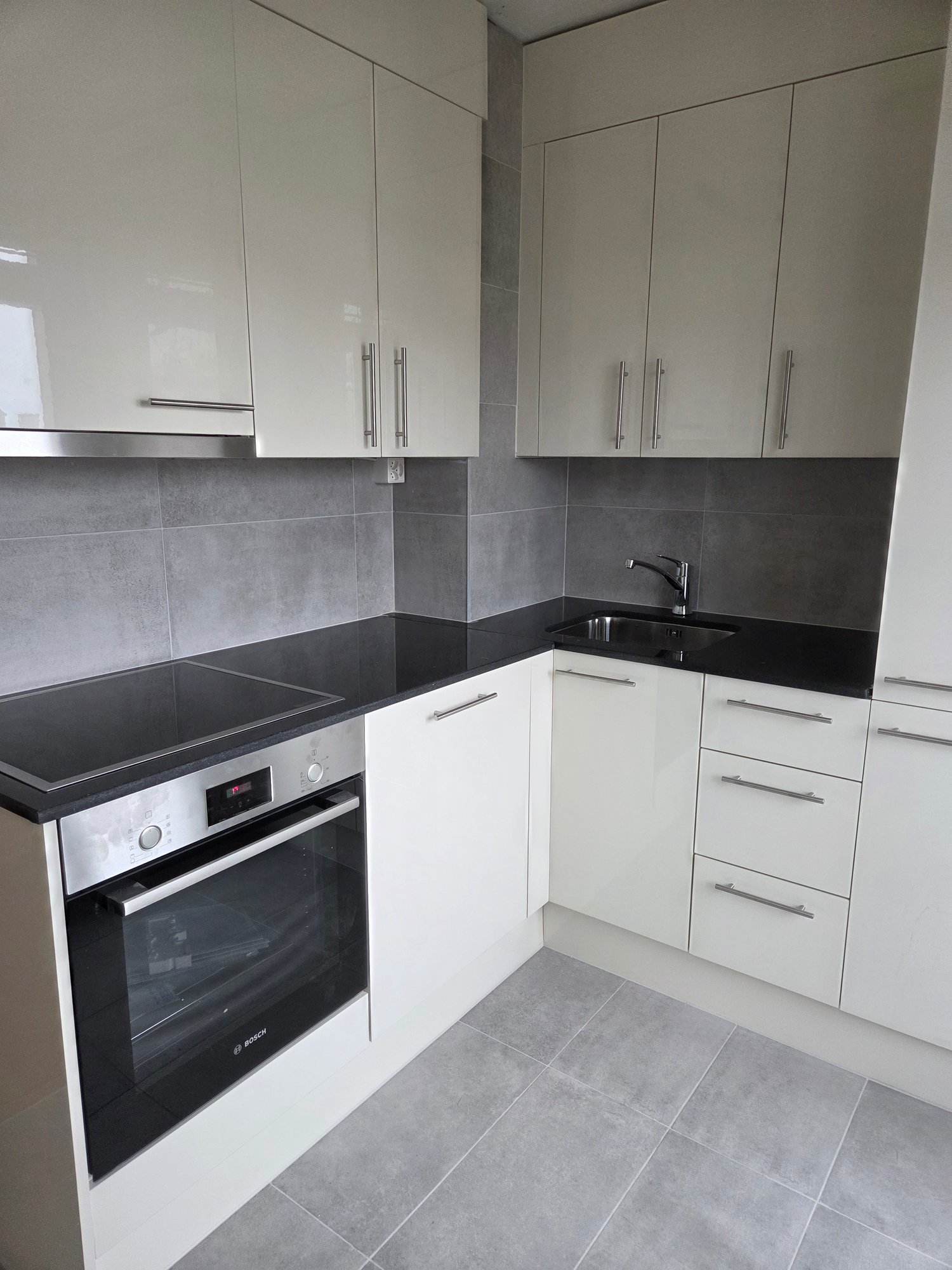 Modern fitted kitchen with white cabinets, black countertops, silver appliance and tile floor