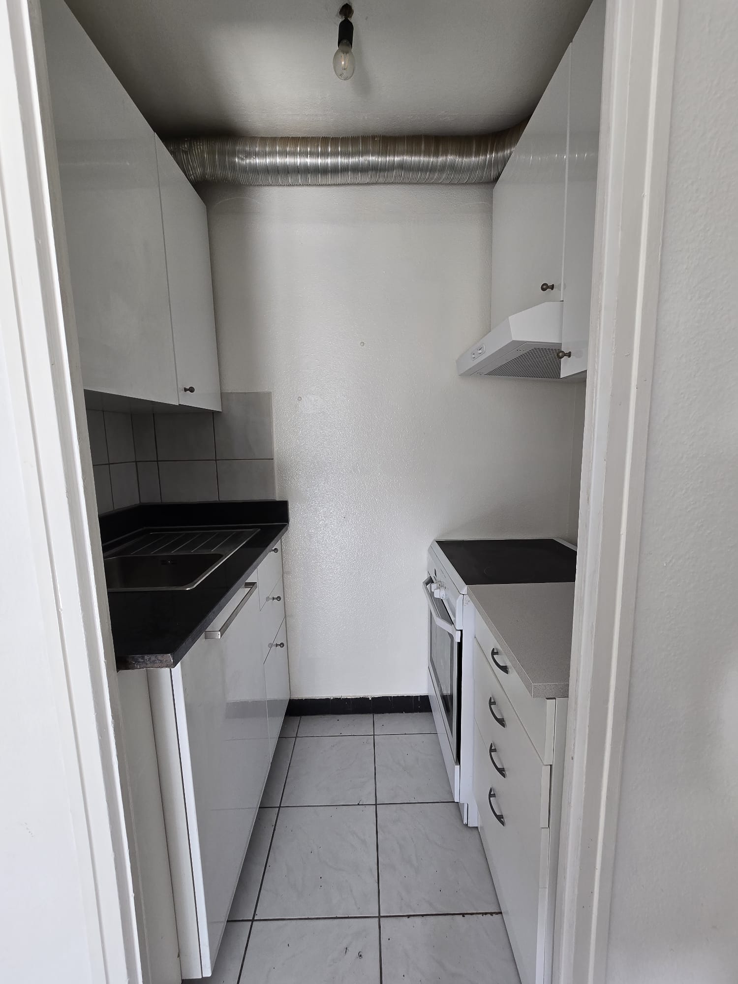 modern kitchen with white cabinets, black countertops, white tiled floor, white appliances, extractor hood, light fixture