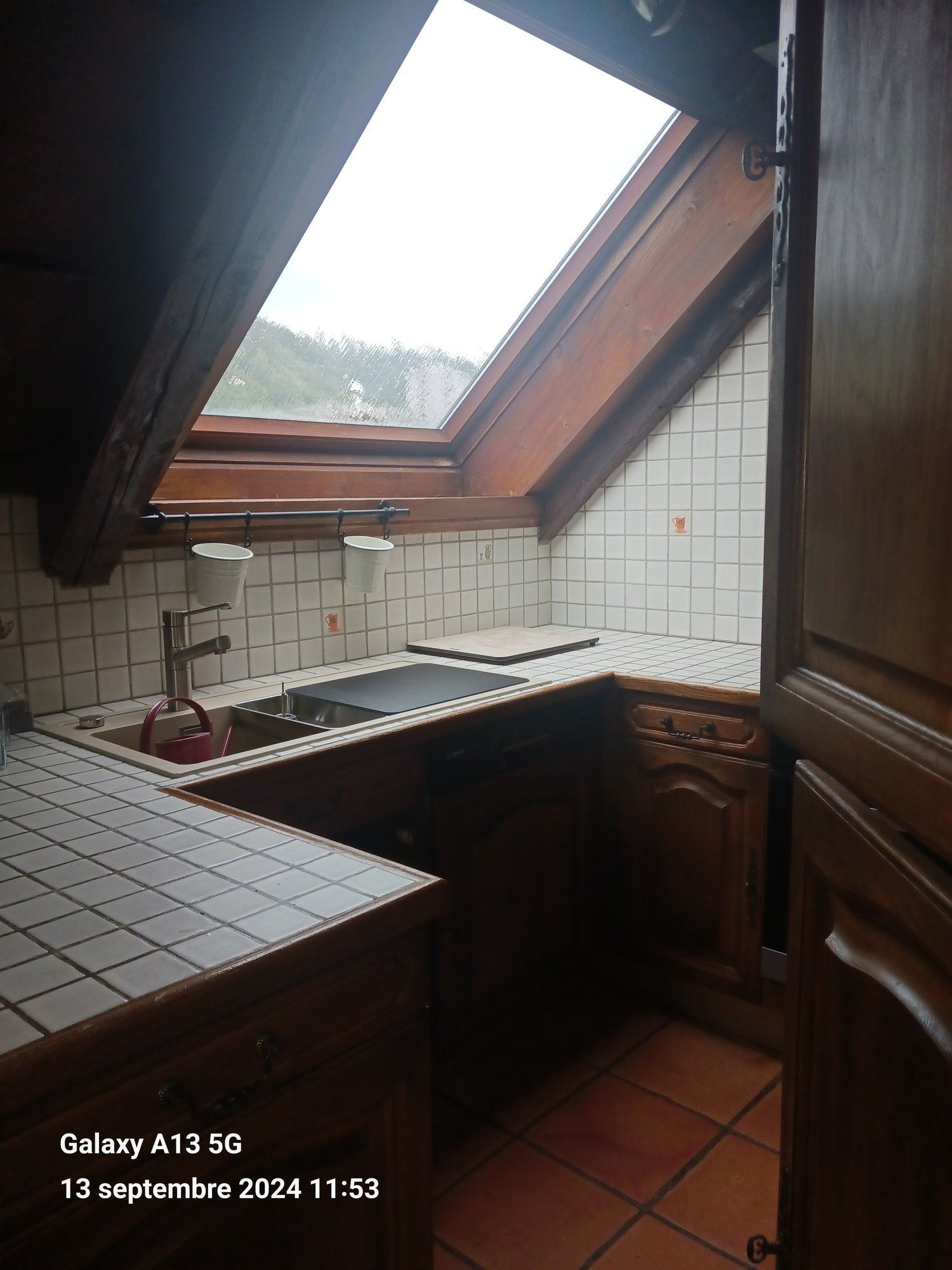 kitchen with sink, faucet, chopping board, wooden cabinets, tiled floor, attic window