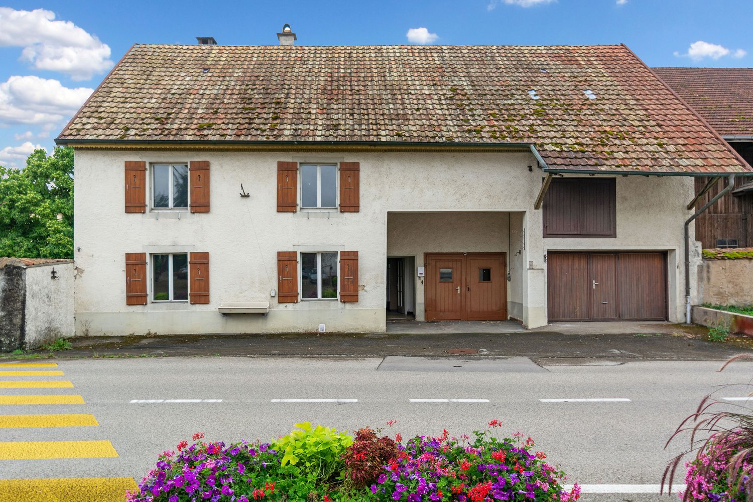 white house, brown tiled roof, brown wooden shutters, two garages, entrance