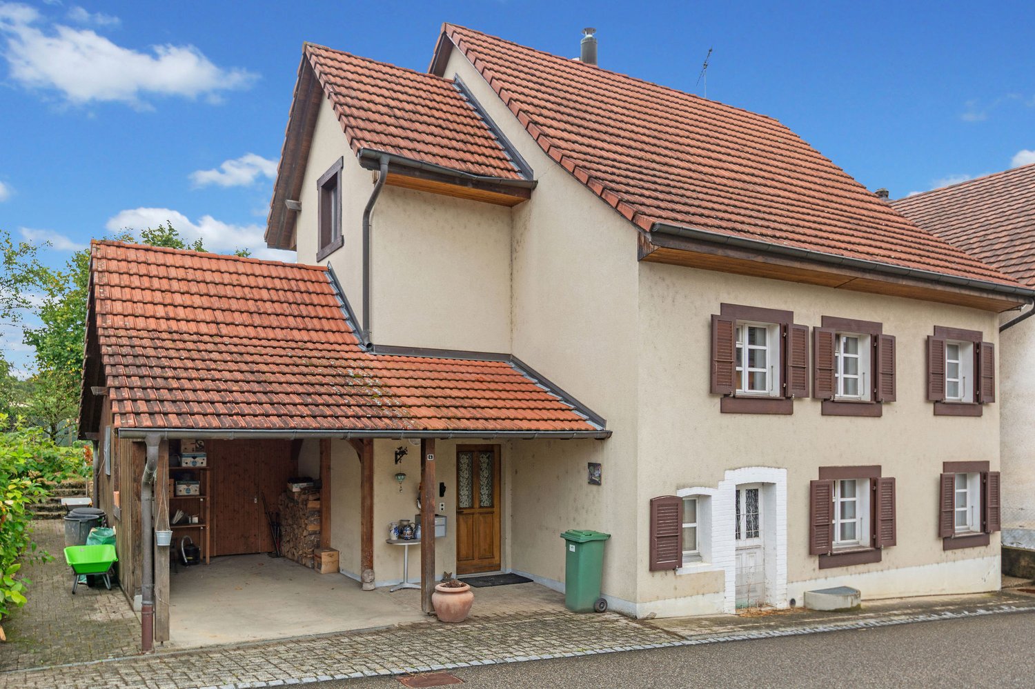 Two-story house with red roof, beige walls, wooden windows, attached garage, brick driveway.