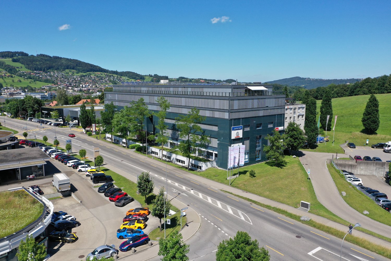 large office building, multiple parking lots, solar panels on the roof, trees and grass surrounding