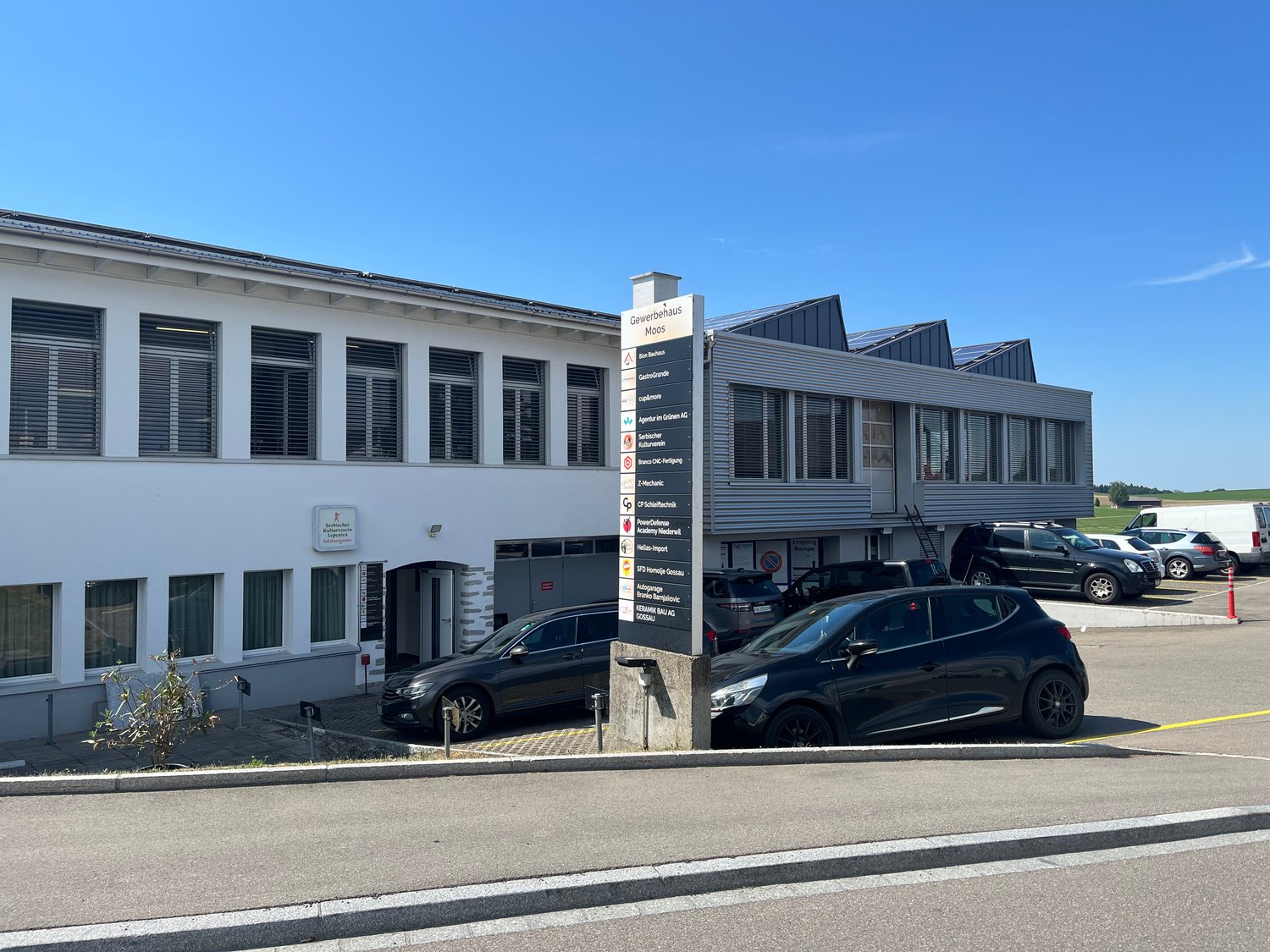 2-story commercial building with signage indicating it is a business center, several cars parked in the lot in front of the building