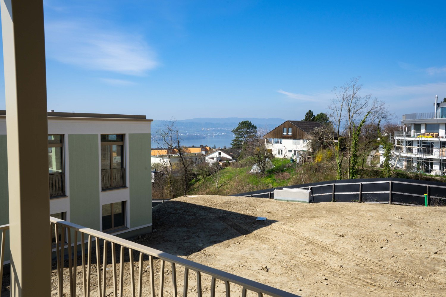 Building with balcony, overlooking a hill with houses and a lake in the distance