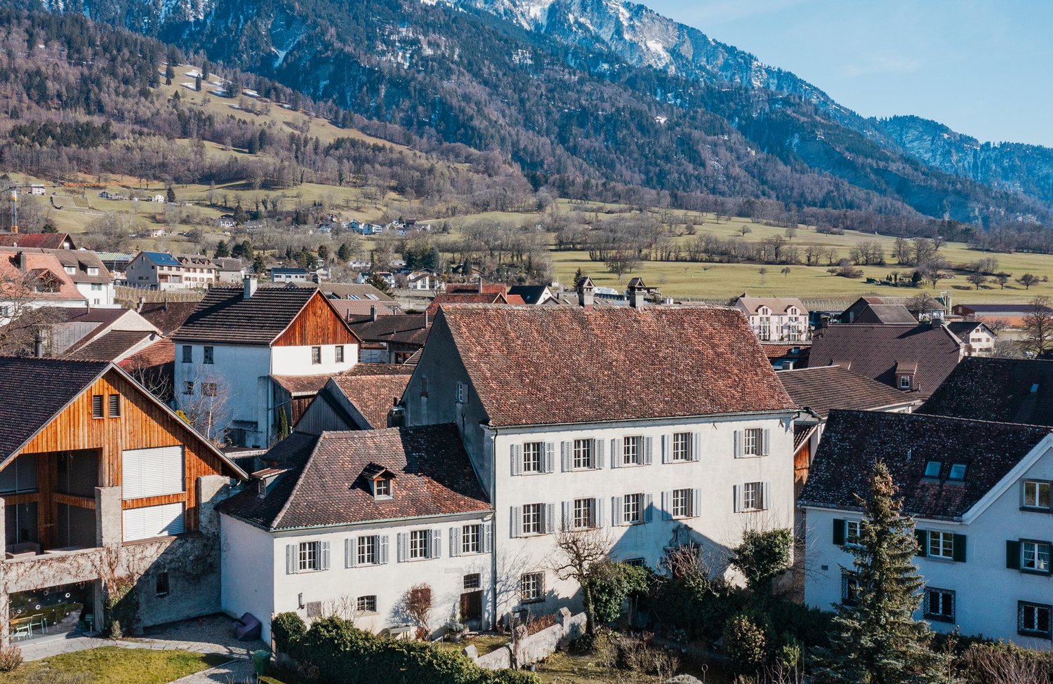 Various houses with different roofs, some with balconies, surrounded by greenery and mountains