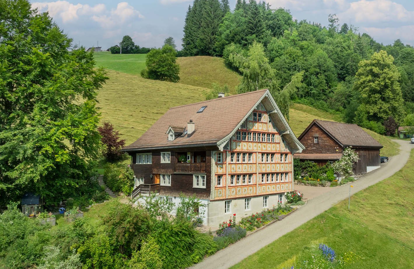 Detached house with a brown roof, surrounded by greenery, wooden accents, and large windows.