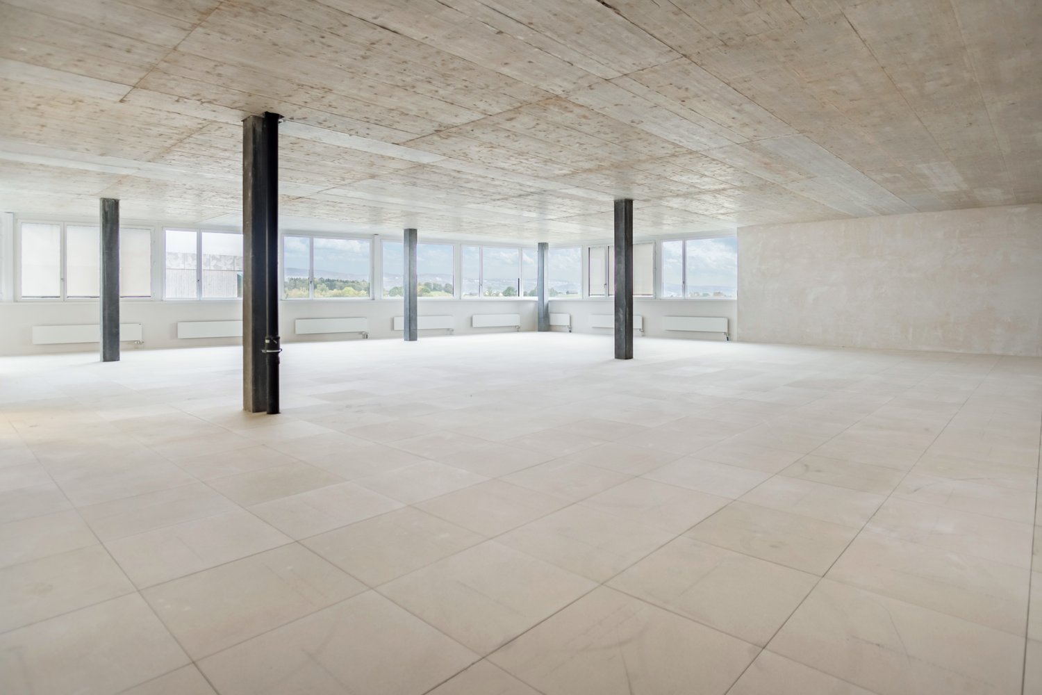 large room, white tile flooring, concrete ceiling, exposed beams, large windows