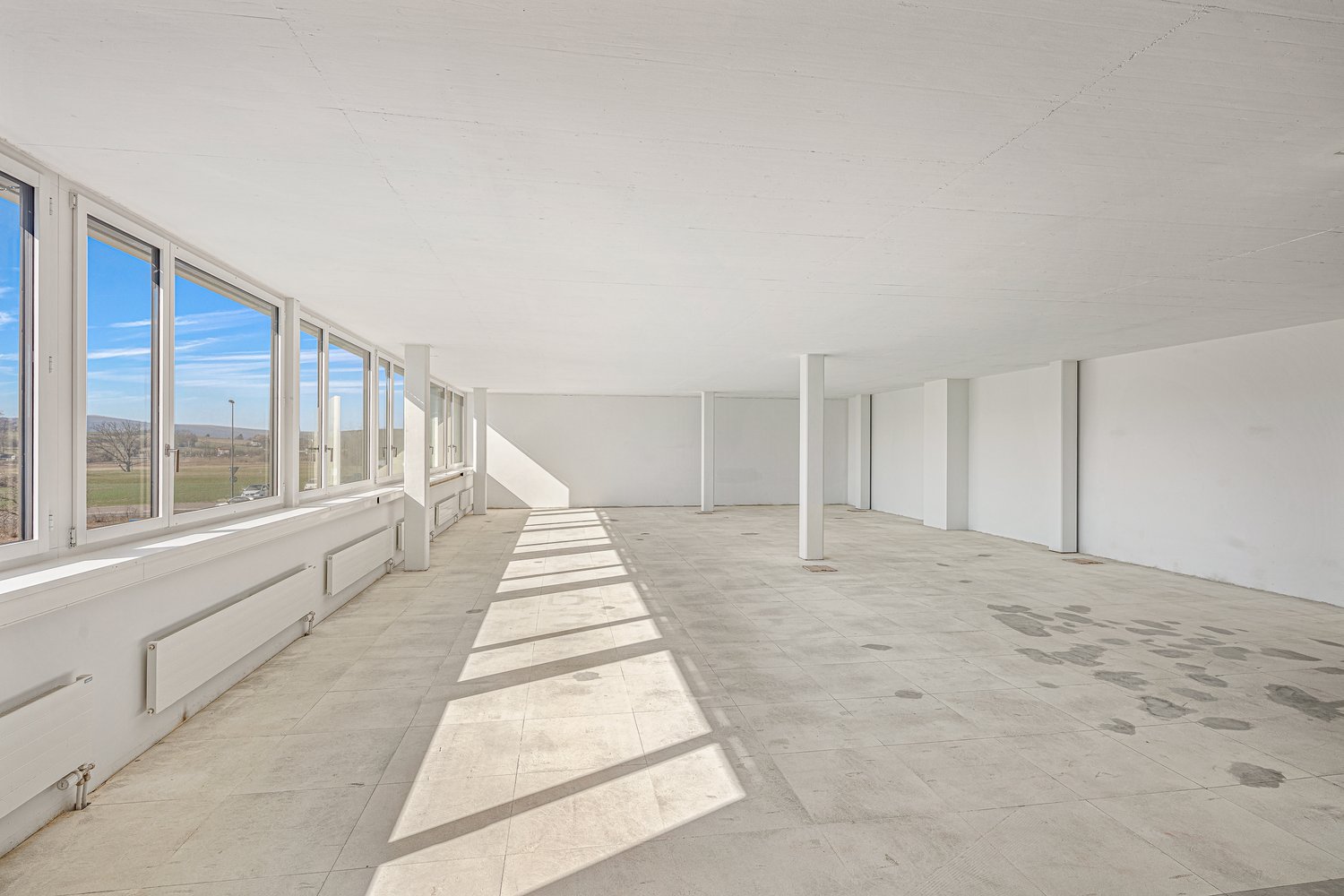 Empty room with large windows, tile flooring, white walls, white ceiling, pillars