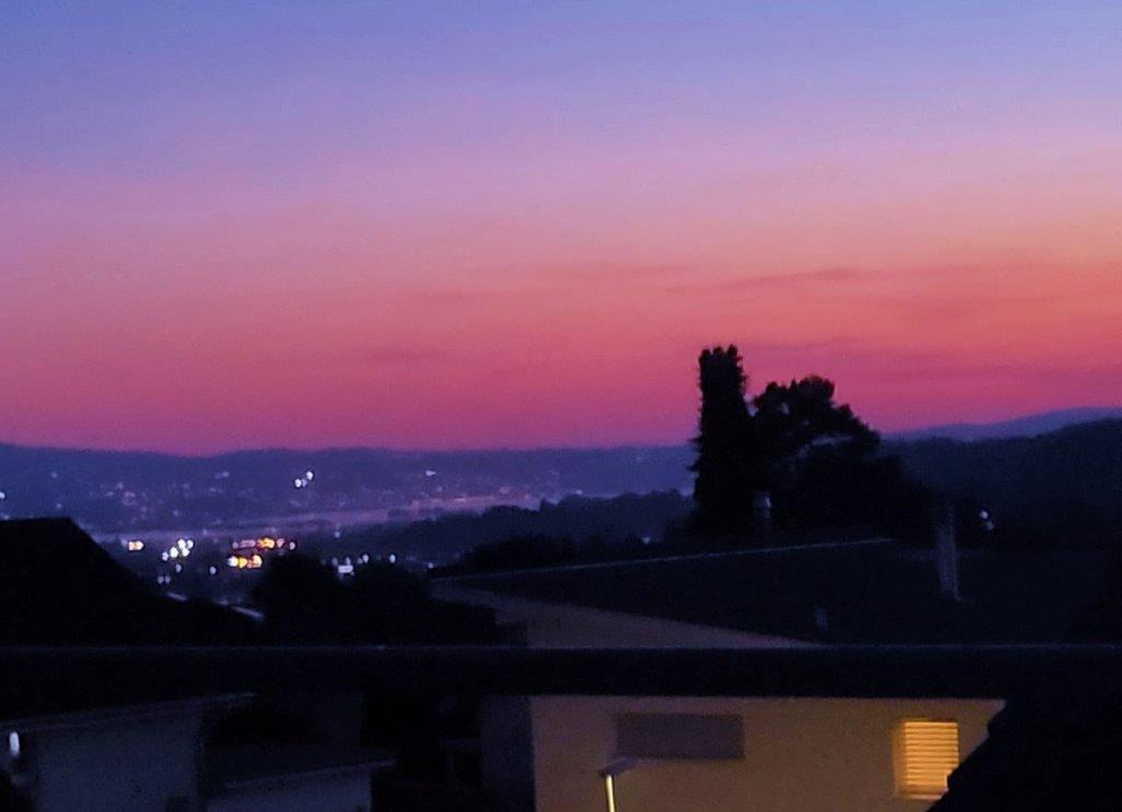 Sunset view from a balcony, cityscape, mountains, trees, and a clear sky