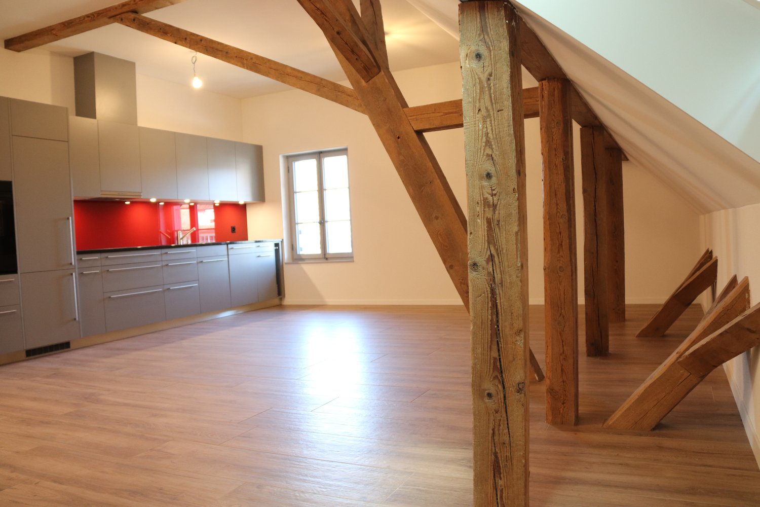 attic kitchen with wooden beams, white walls, wooden floor, modern cabinets, glass window, red tiles, silver appliances