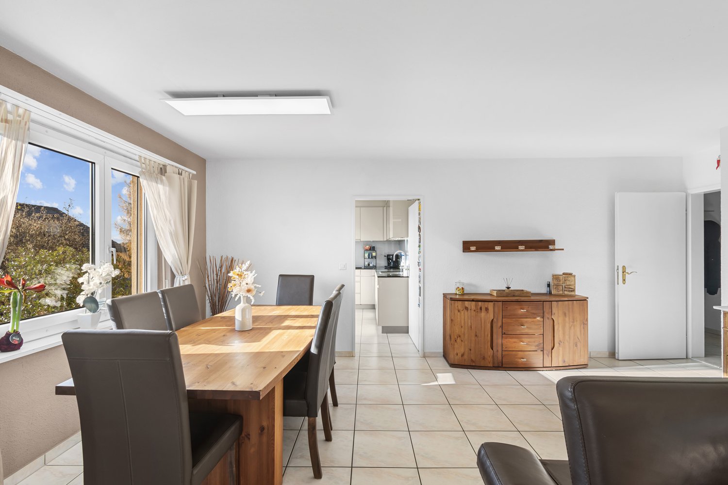 large windows, wooden dining table, chairs, wooden cupboard, bright kitchen