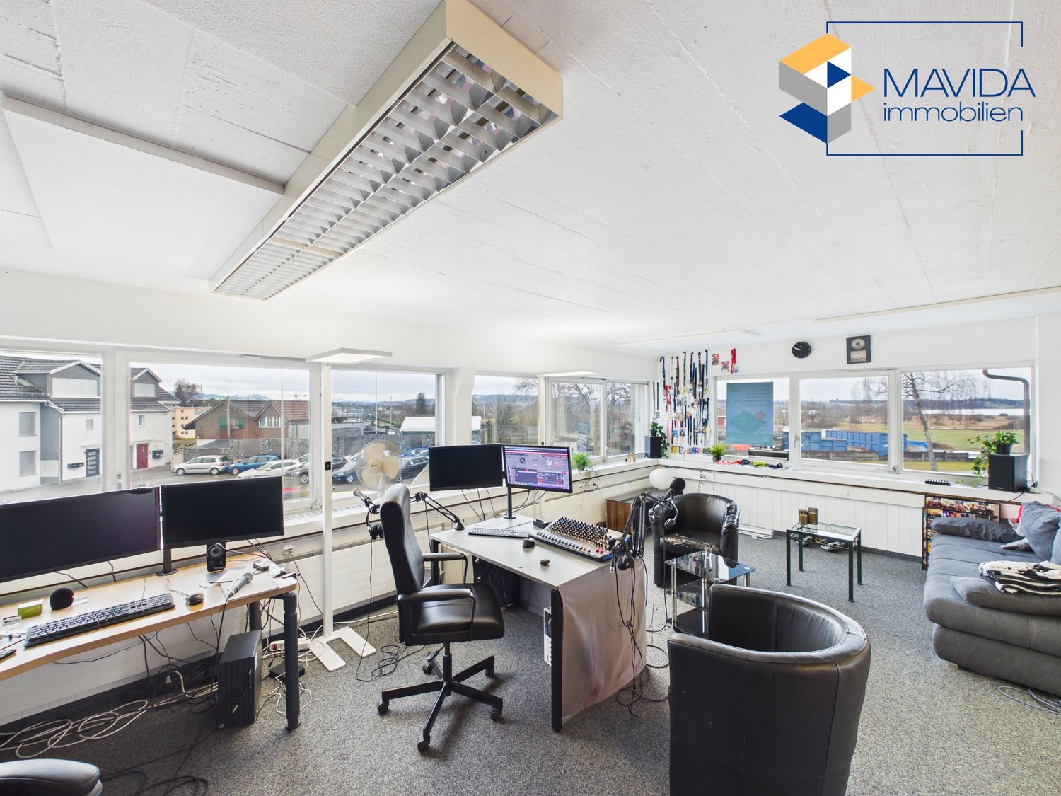 Office with large windows, large desk, 2 computer monitors, black office chairs, couch, and modern decor