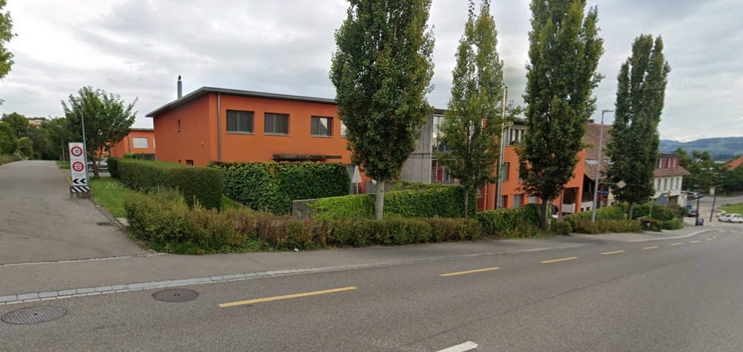 Orange residential building on the street, hedges on the side of the street, trees and bushes around.