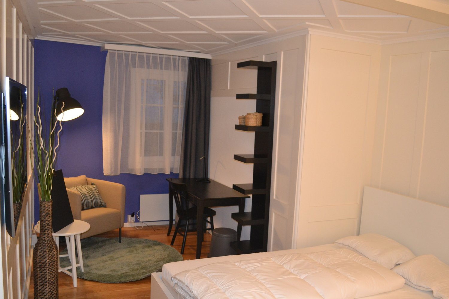 A cozy room with wooden floor, a bed, a desk, a chair, a couch, and a lamp