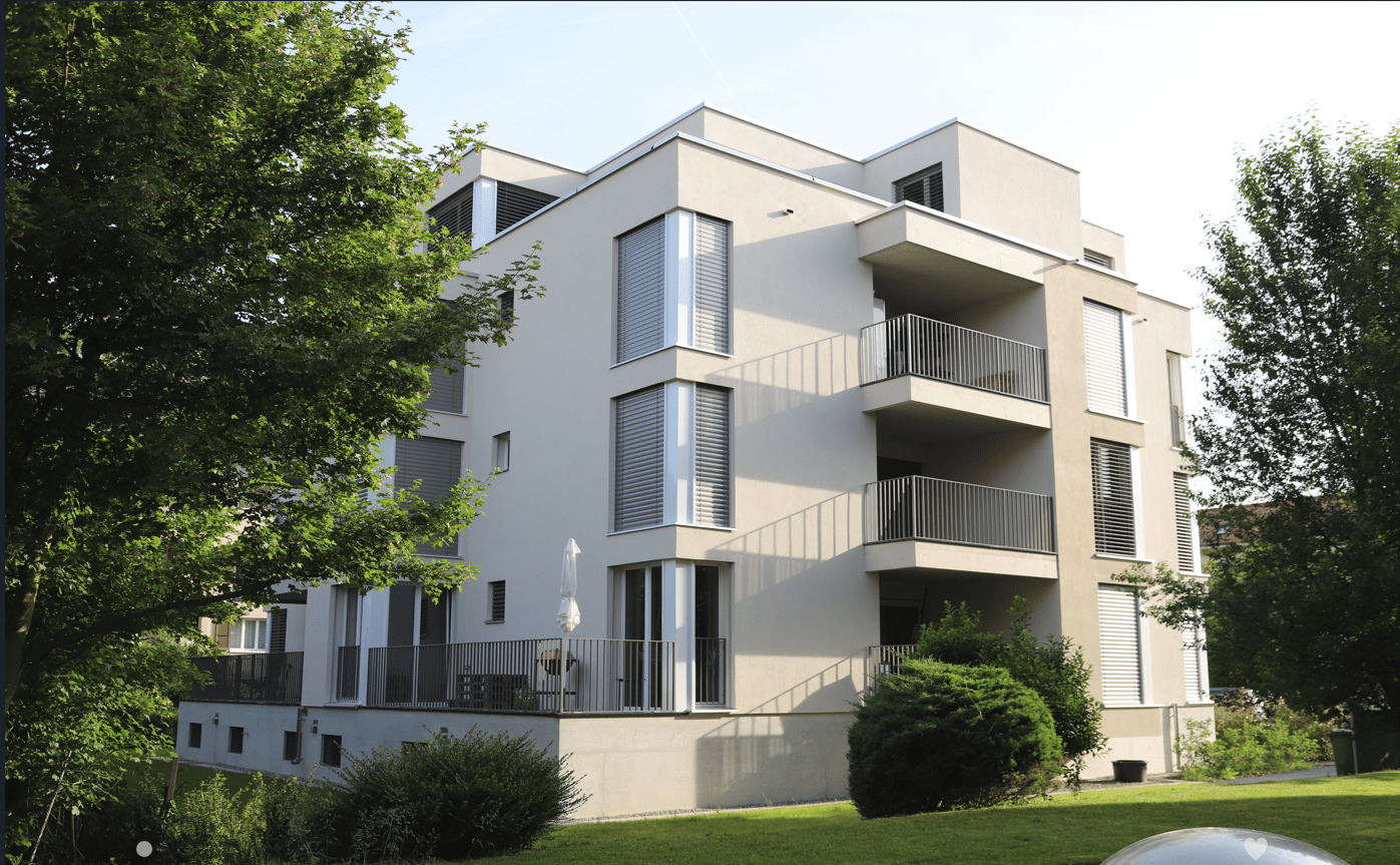 modern apartment building, white exterior, multiple balconies, green surroundings