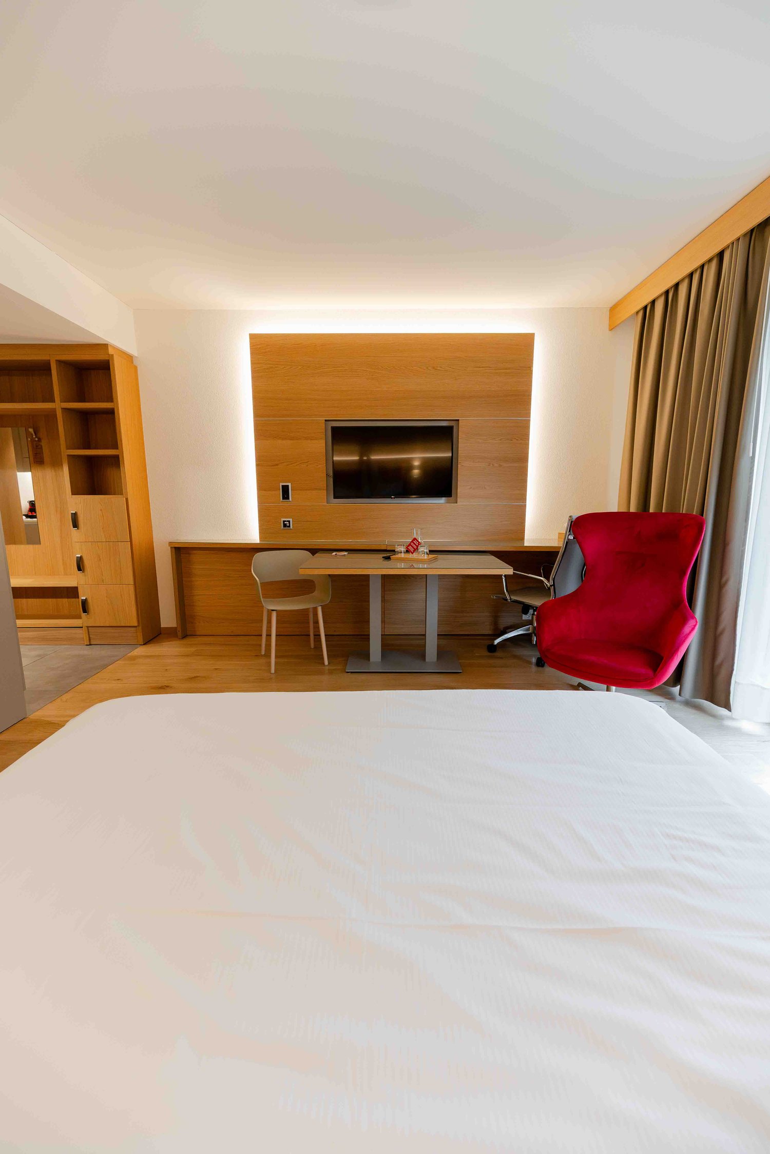 A bedroom with a large bed, a desk, a TV, and a chair.