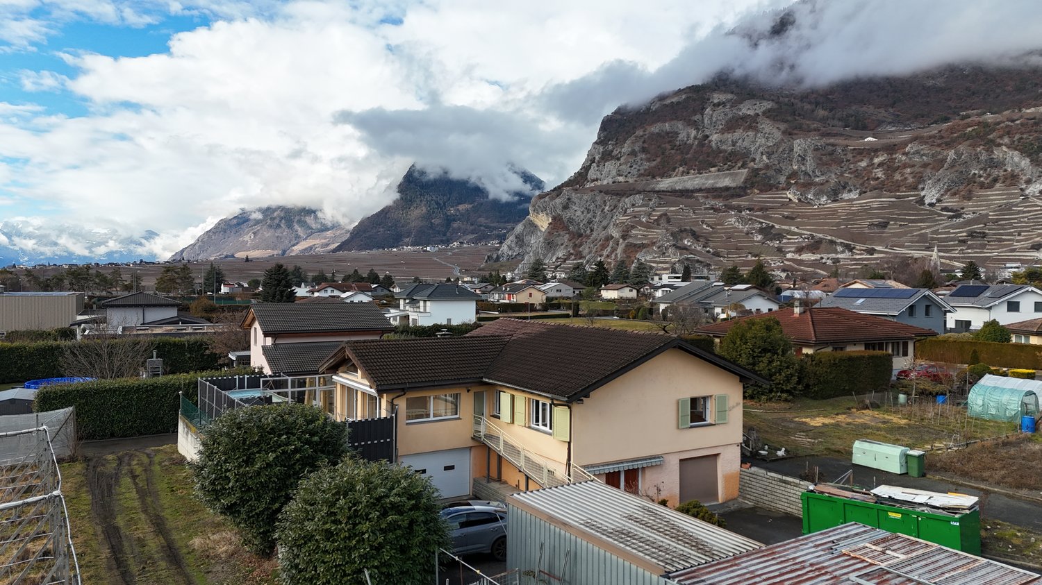 Detached house, brown roof, large yard, garage, located in a hilly, rural area, mountains in the background