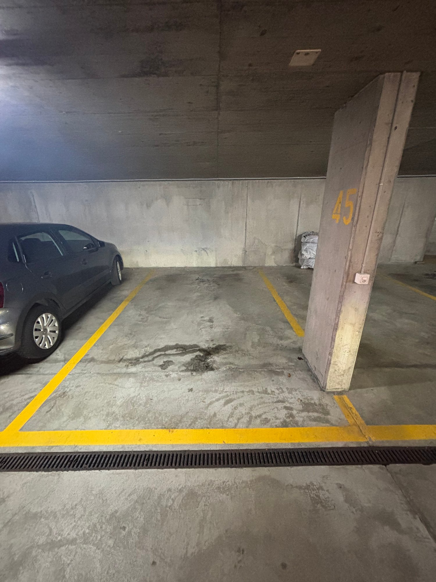 Number 45 parking space, grey car parked, yellow markings on floor, concrete walls, drainage grate