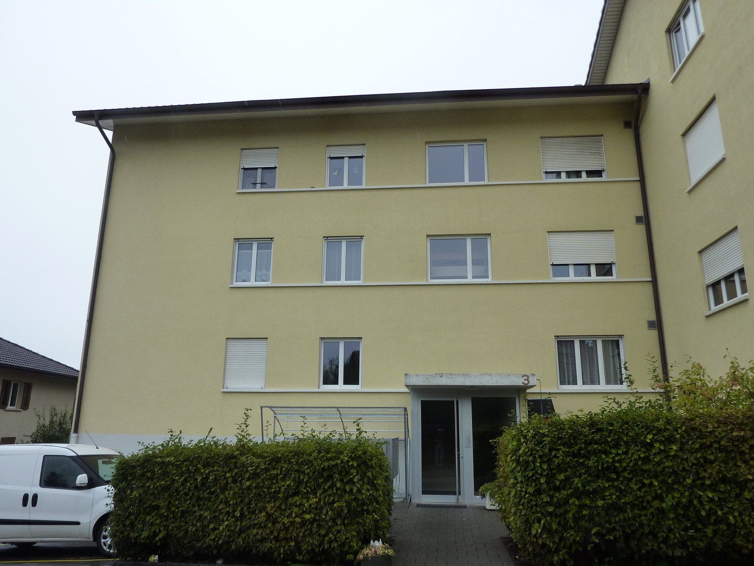 3-story yellow building, multiple windows, entrance with glass doors, white van parked in front