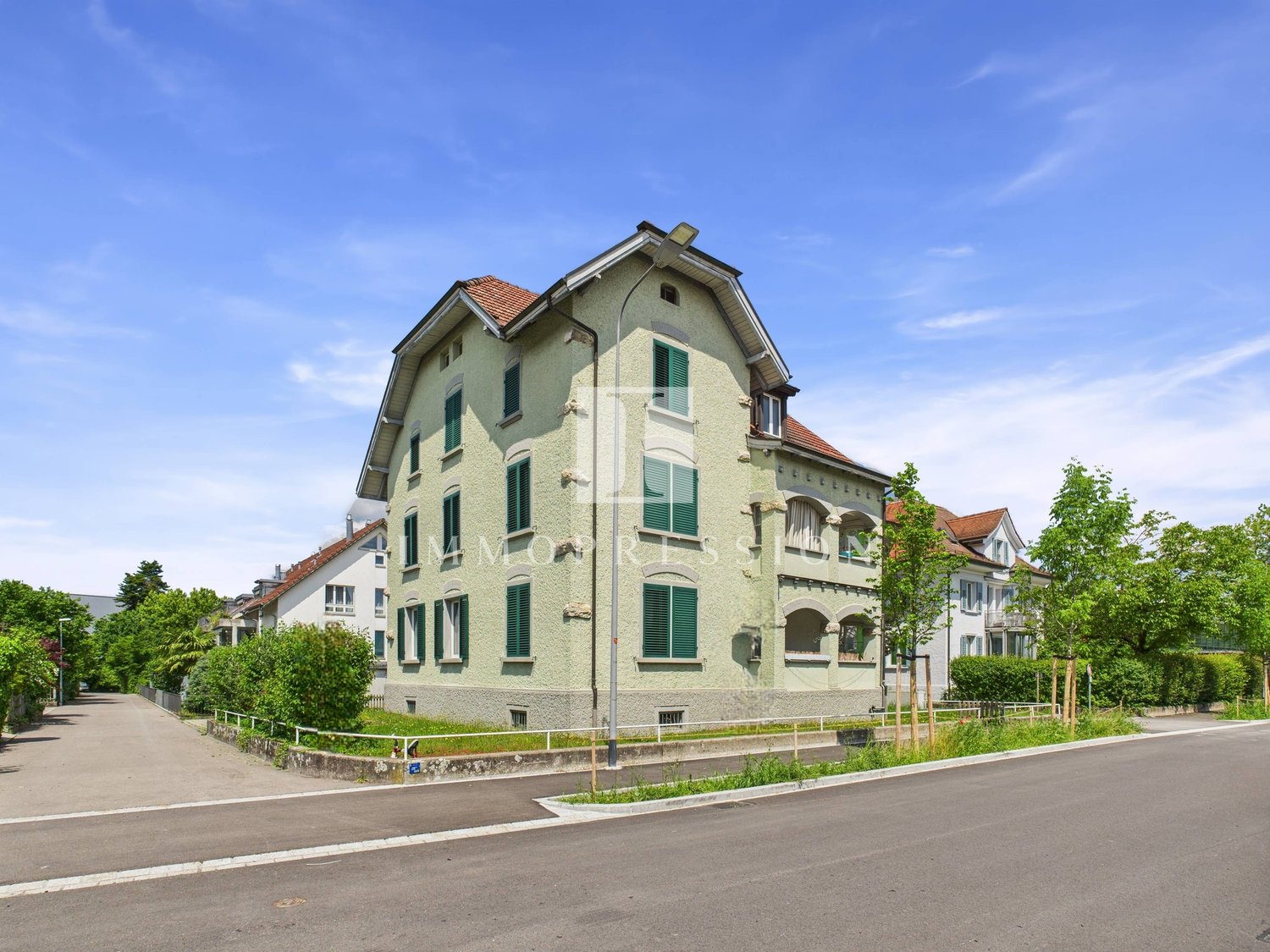 Two-story building, red roof, green shutters, white trim, driveway, trees, bushes, streetlight