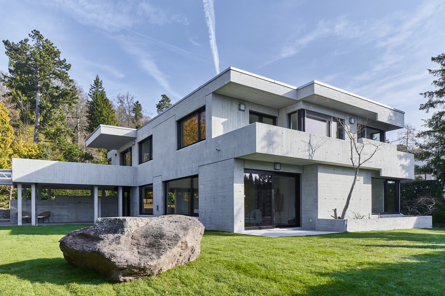modern concrete house, large windows, balcony, large rock in front