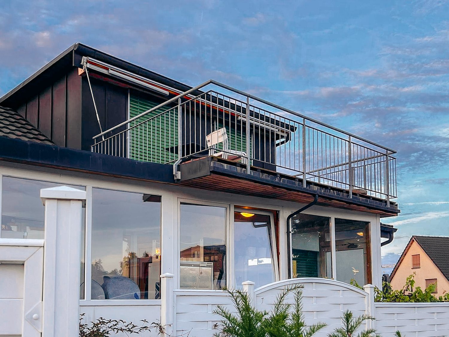 white house, black roof, balcony with metal railing, glass windows, white fence