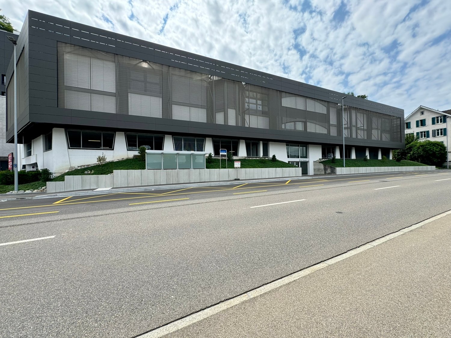 Modern office building with glass windows, concrete planters in front, road next to the building