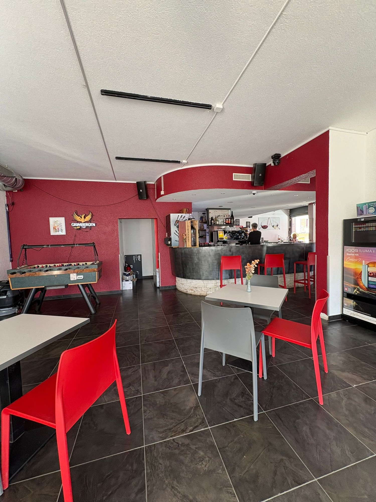 red wall, black tiled floor, counter with chairs, foosball table, two tables with chairs