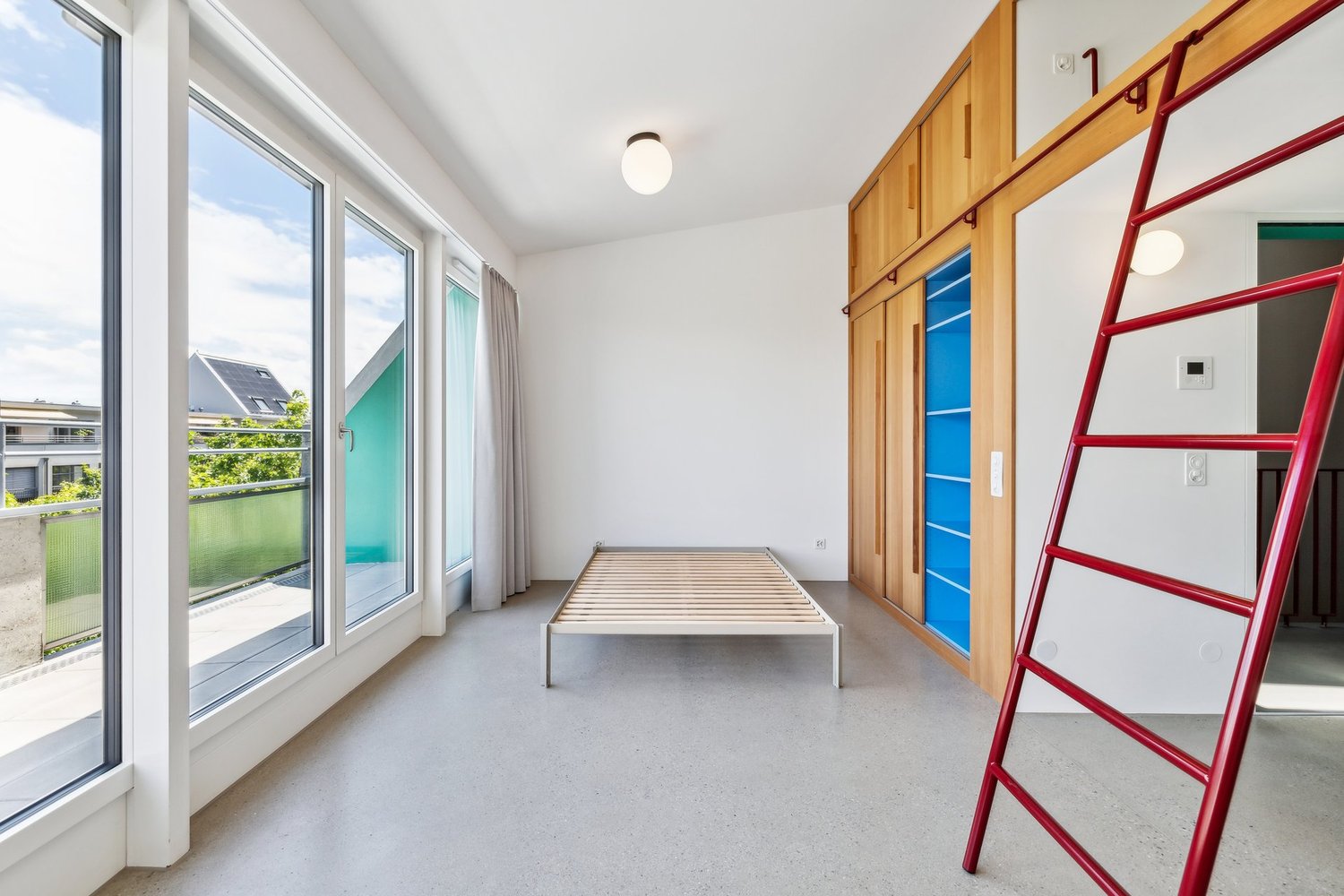 Empty room with a bed, large windows, balcony, wooden ladder, wooden cabinets, white walls, ceiling lamp