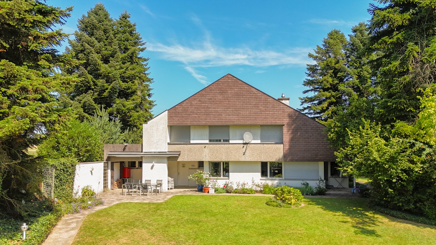 House with brown roof, white walls, large front yard, outdoor seating area, plants, trees, fence