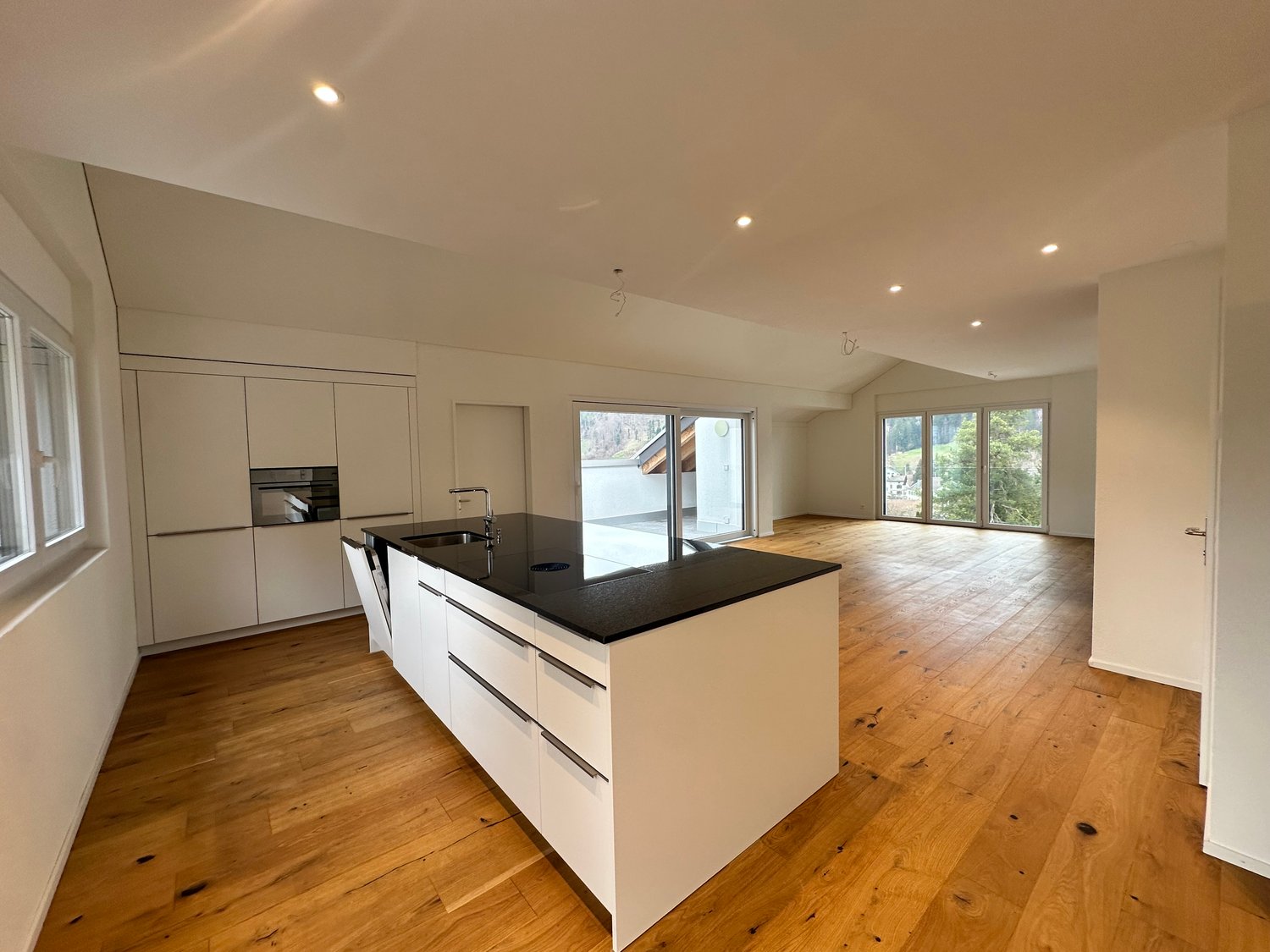 modern kitchen with island, black granite countertop, white cabinets, wooden floor, large windows, balcony