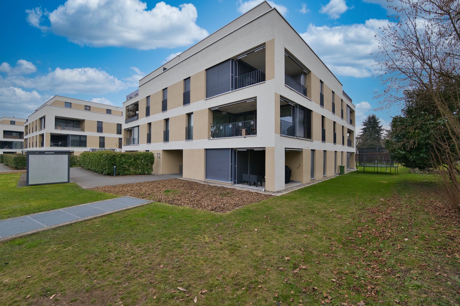 Three story apartment building, balcony on each floor, grey and beige exterior, fenced yard