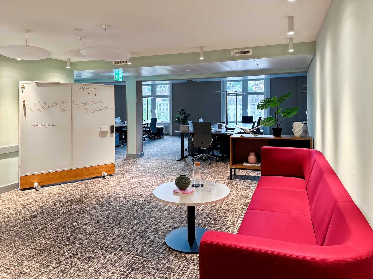 modern office room with white walls, red couch, white table, plants, office chairs, desks, whiteboards