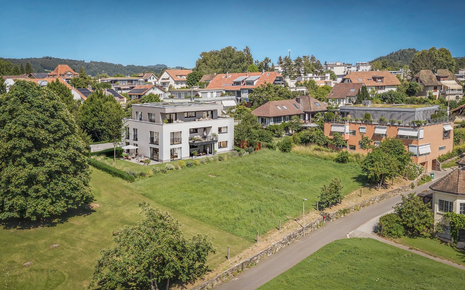 Multiple residential houses in a hilly neighborhood, large front and back yards, some with balconies, greenery and wide roads