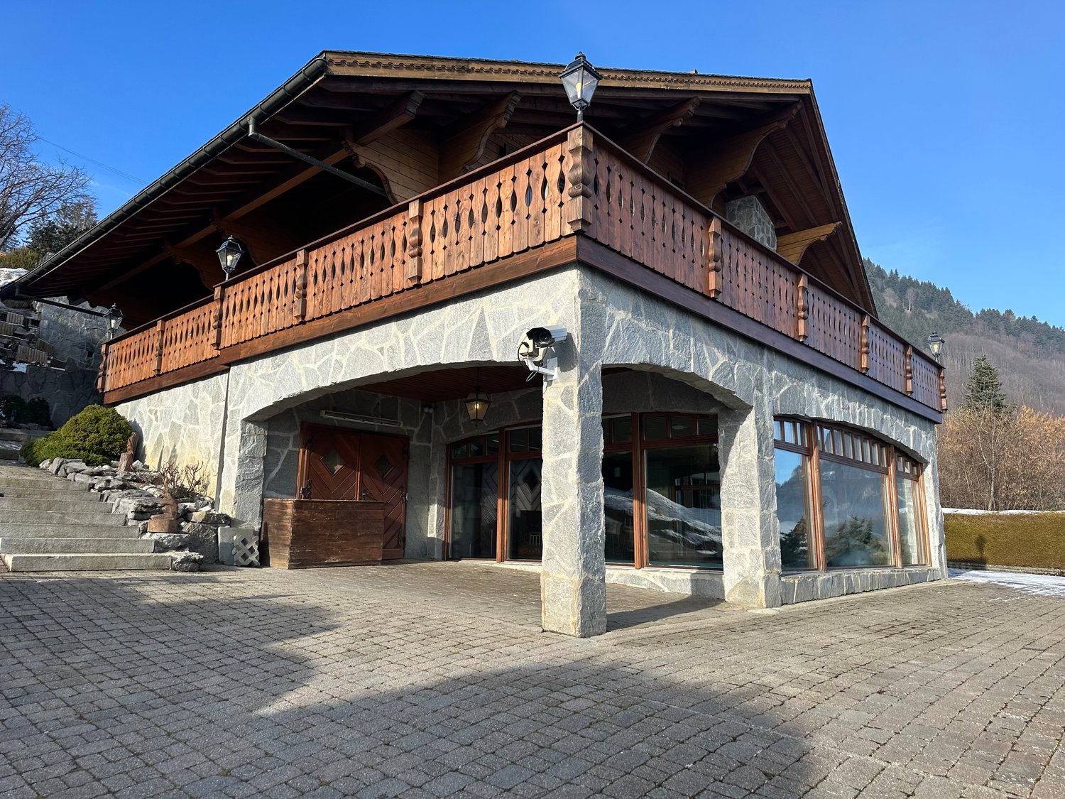 Rustic mountain house with wooden balcony, brick and stone construction, double entrance, security camera, brick driveway