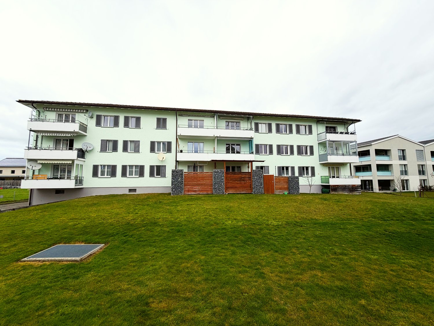 3 story apartment building, green exterior, multiple balconies, large grassy area in front