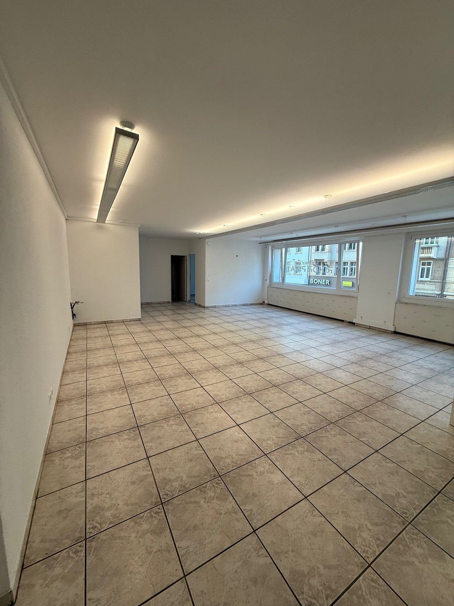 large empty room, tiled floor, white walls, single entry door, long fluorescent ceiling light