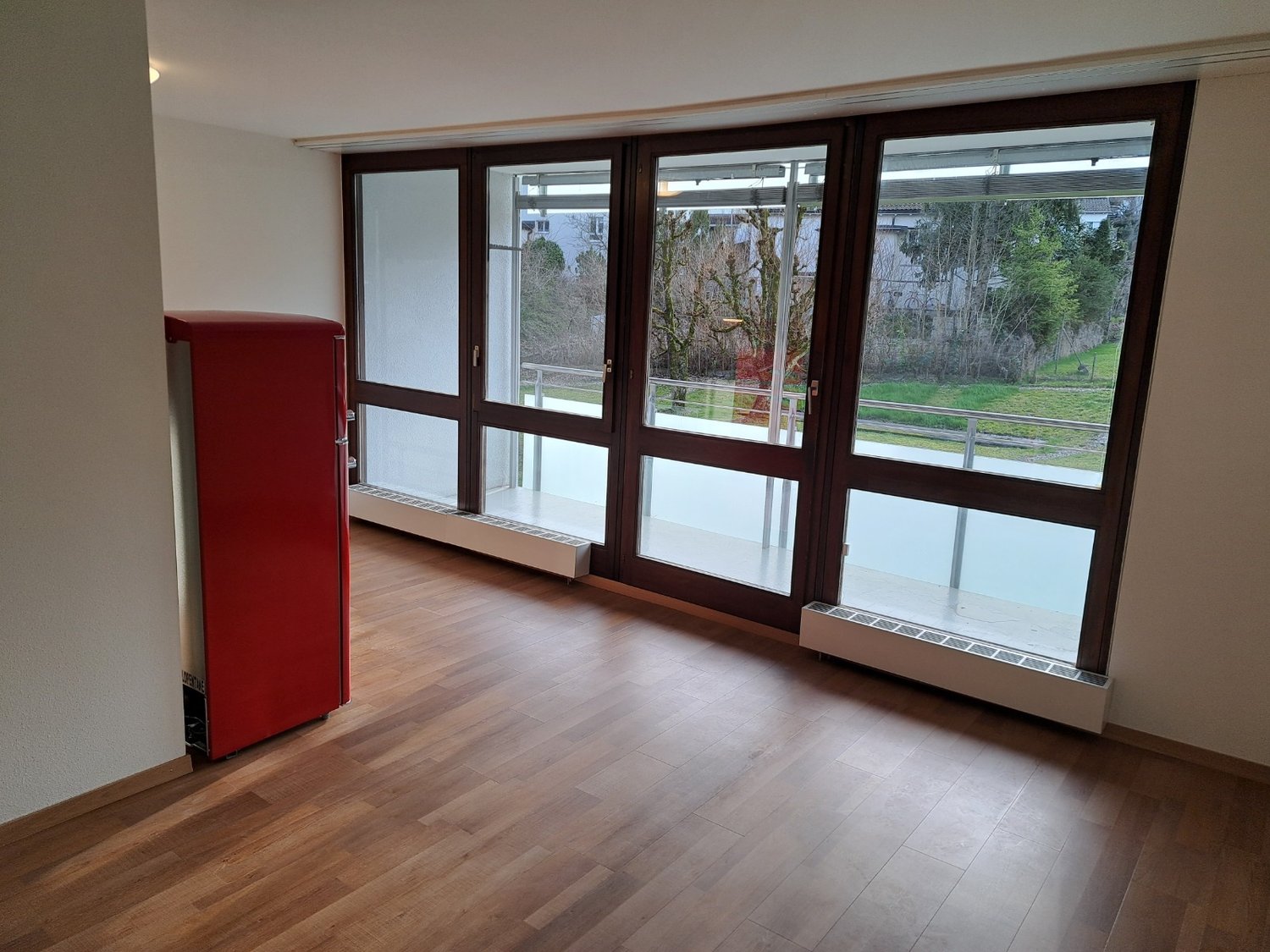 room with glass doors leading to balcony, wooden floor, white walls, red refrigerator