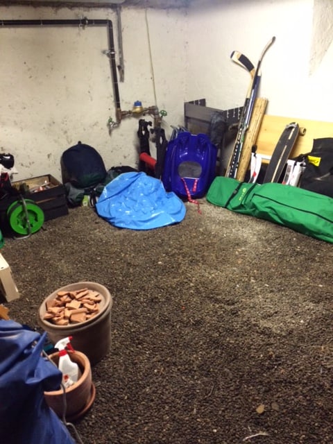The image shows a cluttered garage space with various items such as tools, equipment, and storage containers scattered around the floor.
