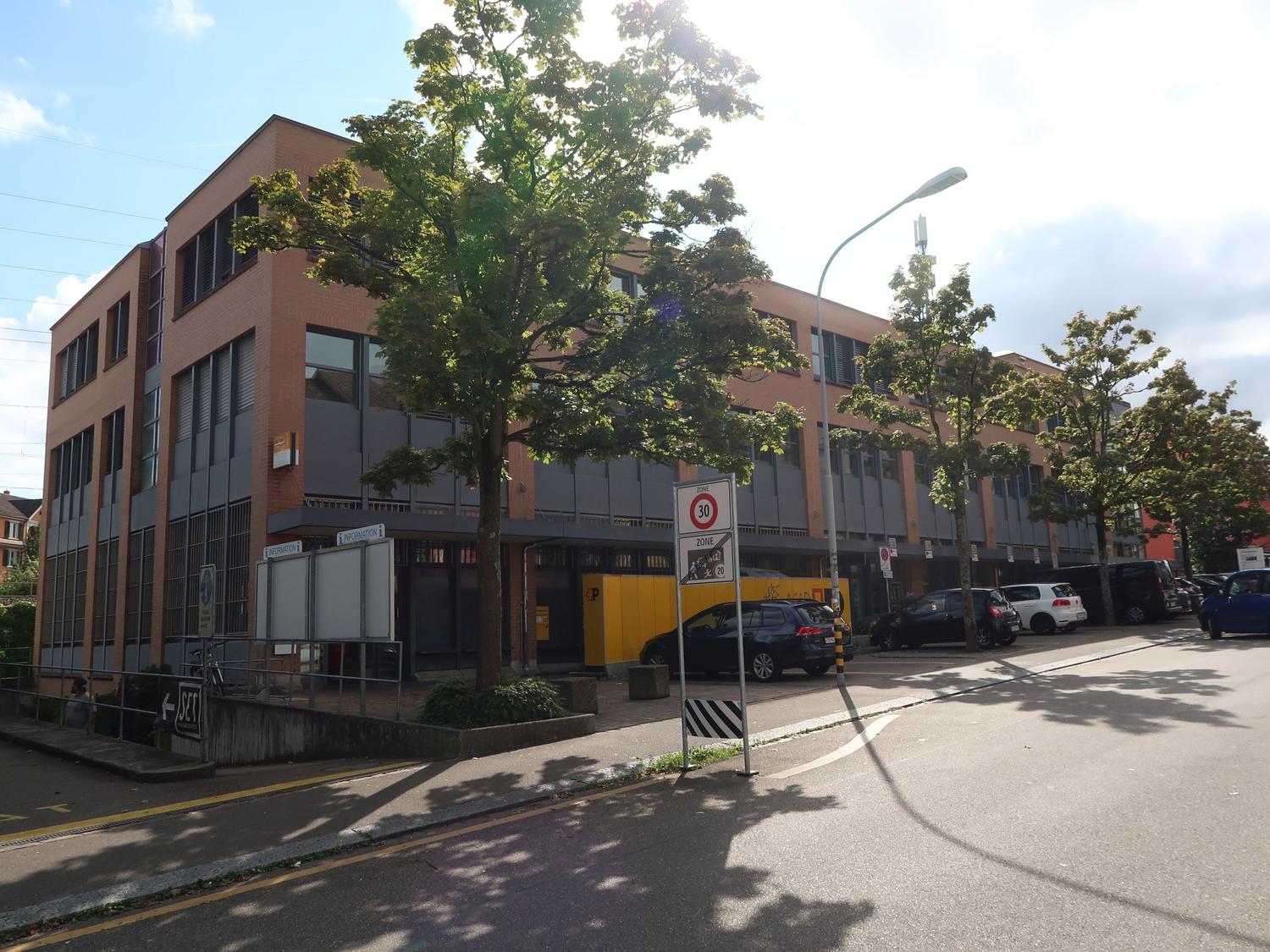 3 story office building, red brick, multiple windows, parking lot, trees, speed limit sign