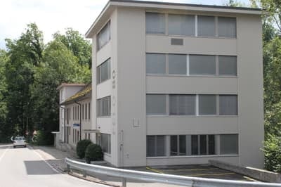 4 story building, white, double glazed windows, metal barrier, parking lot, trees