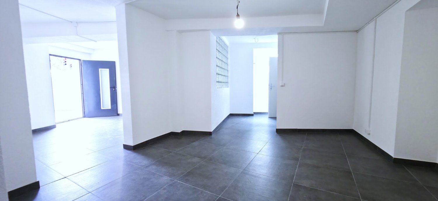 Empty room, white walls, black tiled floor, two doors, one with glass panel