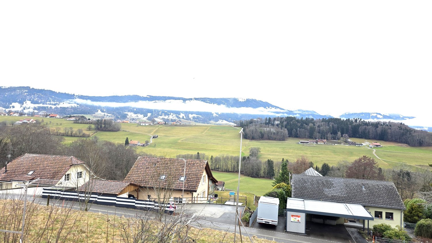 Aerial view of several houses, green fields, mountains in the background